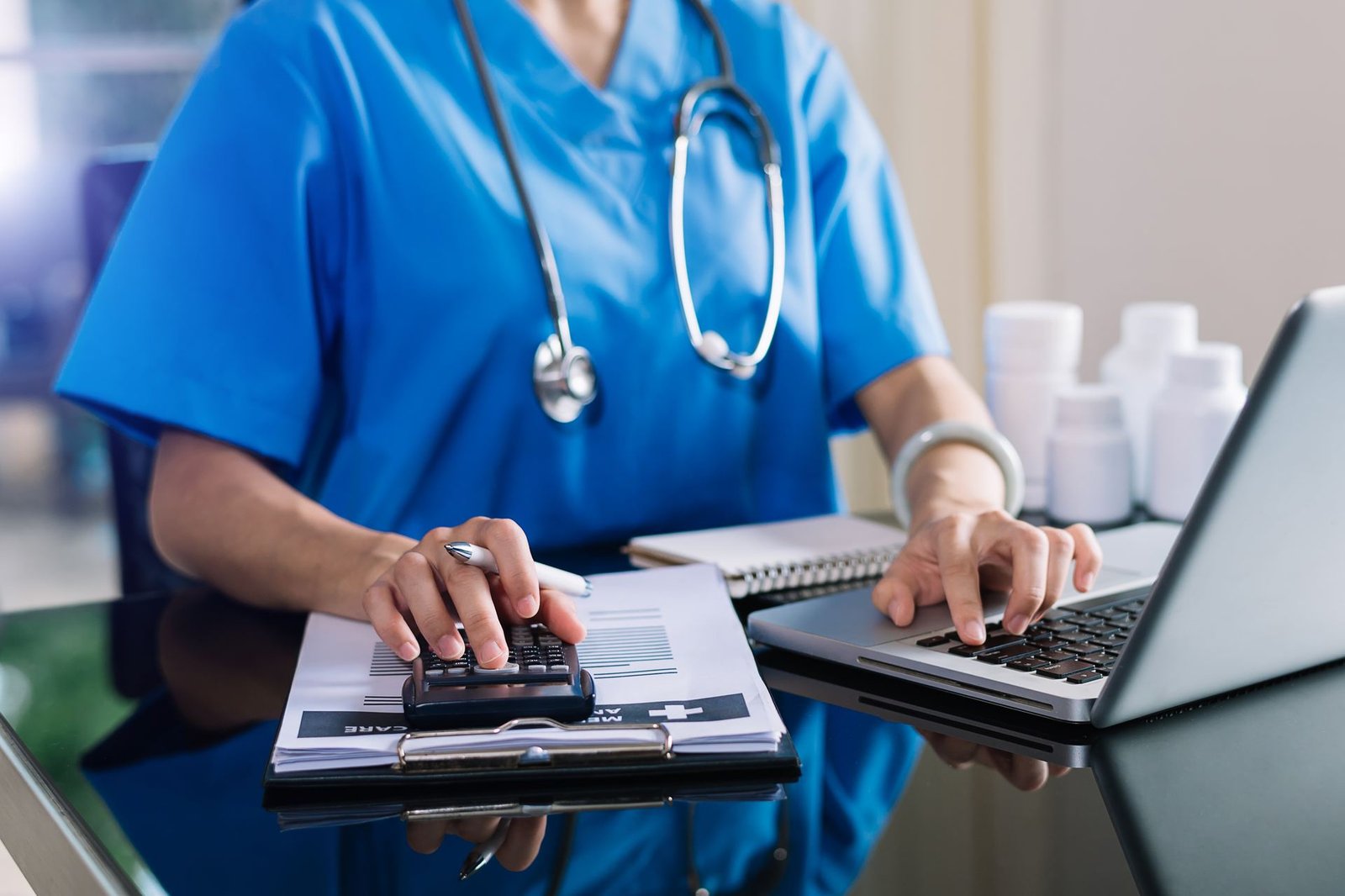 Clinical staff reconciling balances with a calculator and laptop